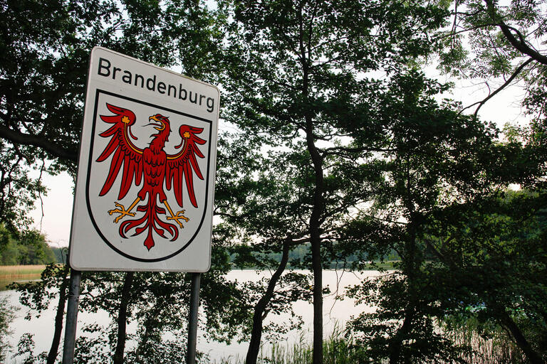 Schild Bundesland Brandenburg mit typischer Seenlandschaft im Hintergrund